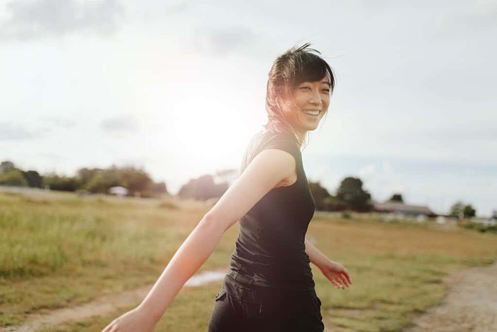 Outdoor shot of smiling young woman runner looking at camera. Chinese female walking on field in morning.