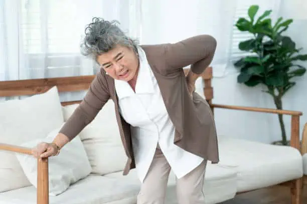 Senior Asian woman suffering from backache at home.