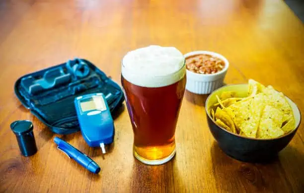 Diabetes and alcohol. Diabetes test devices with a pint of beer and snacks.