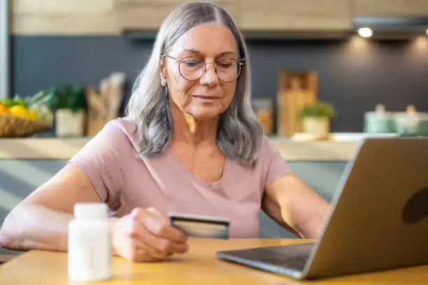 Senior woman holding credit card while using laptop in kitchen worktop.