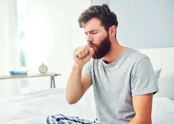 Cropped shot of a young man coughing at home