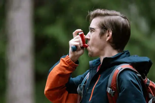 A young man enjoying a nature hike uses his inhaler to help manage symptoms of asthma
